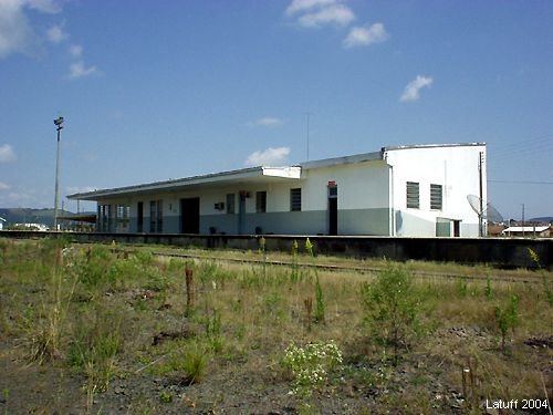 Prédio da estação de Lages visto do pátio, com os trilhos em primeiro plano tomados pelo mato.