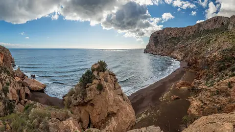 Imagem ilustrativa: Espanha: Praia rochosa com mar calmo e céu nublado